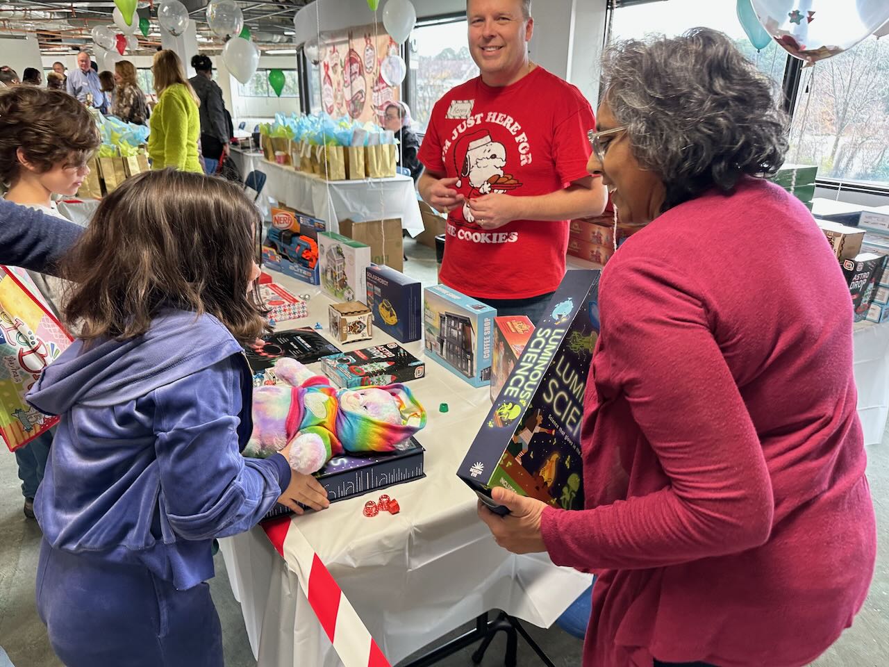 Families browsing tables of toys, games, and gift bags at the gift gathering