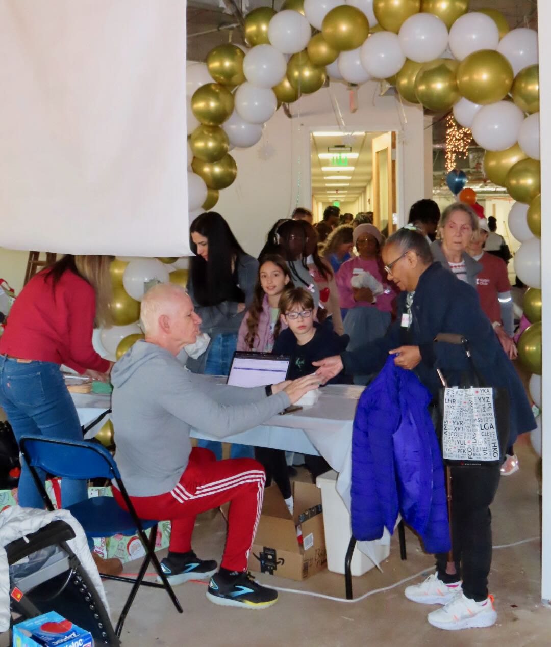 Families arriving at the check-in table beneath an arch of gold and white balloons.